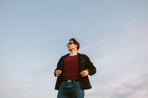 portrait of confident young man standing against blue sky - fashion stock pictures, royalty-free photos & images