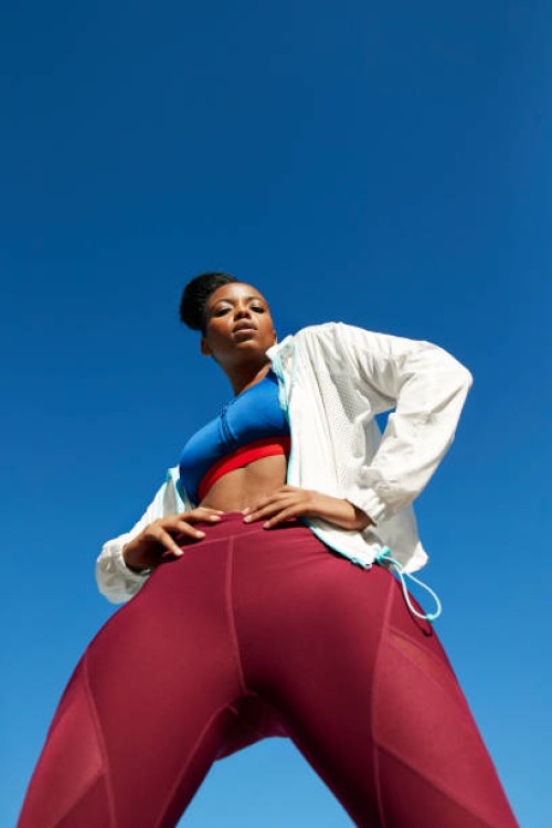 portrait of female athlete with hands on hip standing during sunny day - fashion stock-fotos und bilder