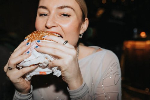portrait of hungry woman taking bite of burger at bar - junk food stock pictures, royalty-free photos & images
