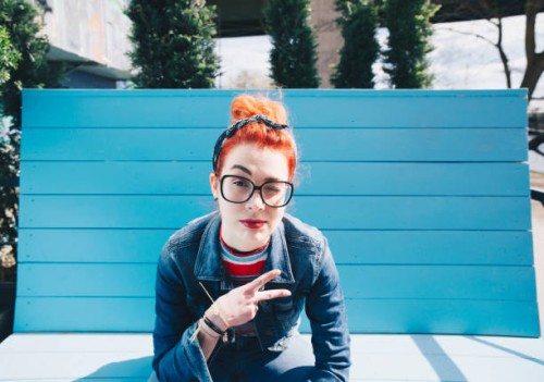 portrait of redhead young woman gesturing peace sign while sitting on bench - fashion stock pictures, royalty-free photos & images