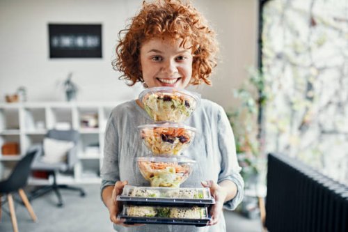 portrait of smiling businesswoman holding stack of takeaway food in office - junk food stock pictures, royalty-free photos & images