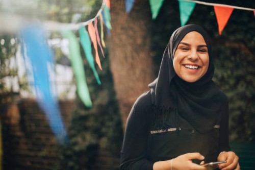 portrait of smiling young woman in hijab holding mobile phone at backyard - garden decoration stock pictures, royalty-free photos & images