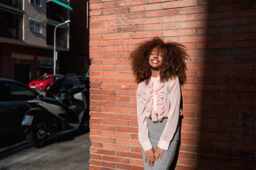 portrait of smiling young woman with afro hairdo leaning against brick wall in the city - fashion stock pictures, royalty-free photos & images