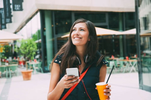 portrait of smiling young woman with cell phone and takeaway drink in the city - junk food stock pictures, royalty-free photos & images