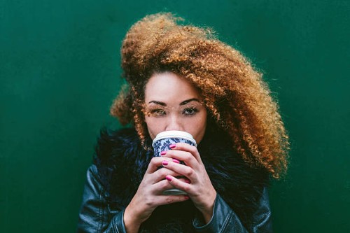 portrait of woman drinking coffee to go in front of a green wall - junk food stock pictures, royalty-free photos & images