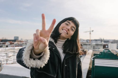 portrait of woman giving peace sign while standing on rooftop - hairstyle stock pictures, royalty-free photos & images