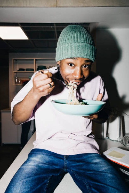 portrait of young man eating noodles while sitting on dining table at college dorm - food stock pictures, royalty-free photos & images