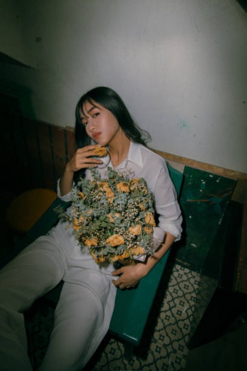 portrait of young woman holding flowers while sitting on chair at home - fashion stock pictures, royalty-free photos & images