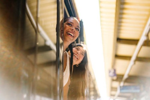 portrait shot of two young women looking out of an open door of a train on a platform and smiling - travel stock pictures, royalty-free photos & images