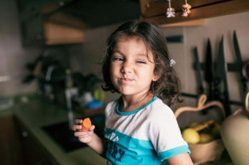 pretty 4 years girl eating carrot in kitchen, sitting on her kitchen counter - food stock pictures, royalty-free photos & images
