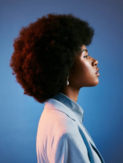 profil de modèle féroce, afro et rétro avec attitude, peau parfaite et coiffure cool, funky et tendance. un portrait puissant d’une femme intense, fière et à la mode sur fond de studio bleu - fashion photos et images de colle