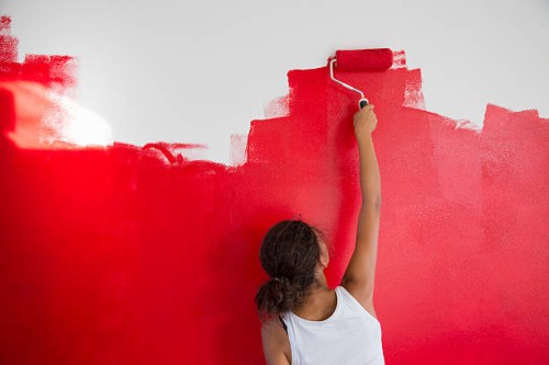 rear view of girl painting red wall with paint roller - home decoration stock pictures, royalty-free photos & images
