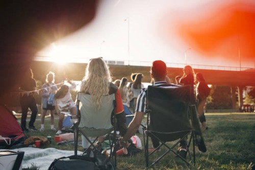 rear view of man and woman holding hands while sitting on chairs in music festival - concert stock pictures, royalty-free photos & images