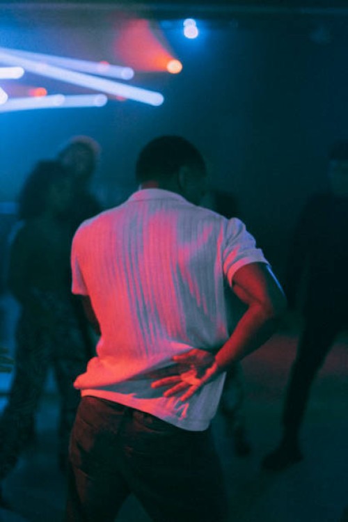 rear view of young man dancing under illuminated red light at nightclub - concert stock pictures, royalty-free photos & images