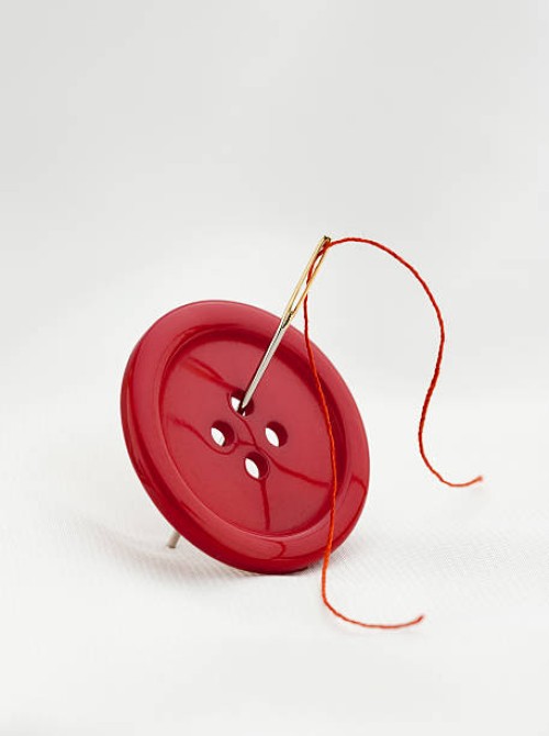 red button with four thread holes and a needle with thread - fashion stock pictures, royalty-free photos & images