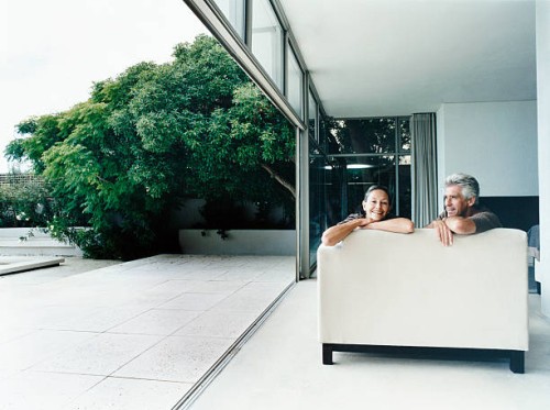 relaxed couple sitting on a sofa in their home with french windows open leading to a garden - garden decoration photos et images de collection