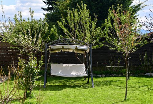 relaxing in the garden swing on a beautiful day, enjoying the peaceful view of the lush green lawn - garden decoration stockfoto's en -beelden