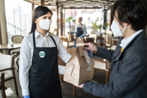 restaurant employee wearing a sticker showing that she has been vaccinated against covid-19, giving a take away food to a customer. - junk food stock pictures, royalty-free photos & images