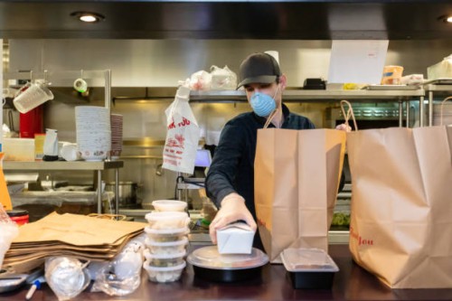restauranteur wearing mask and gloves packaging food for delivery during covid-19 outbreak - junk food stock pictures, royalty-free photos & images