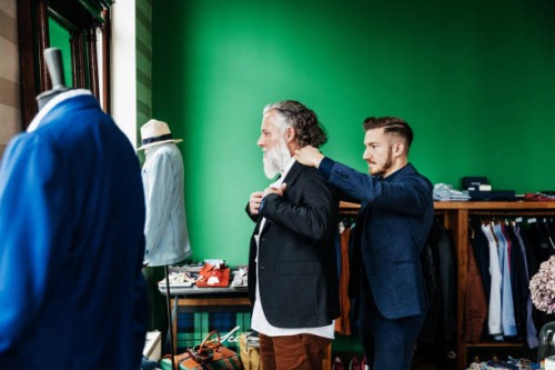 retail assistant helping customer trying on a jacket - fashion stock-fotos und bilder