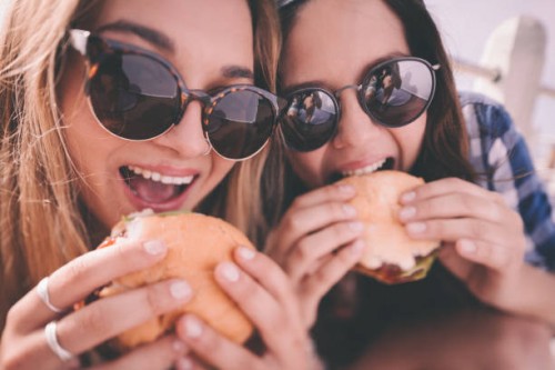 retro style shot of teenage girl best friends eating burgers - junk food stock pictures, royalty-free photos & images