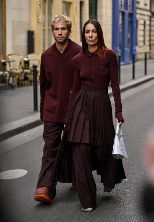 Roques is seen wearing a burgundy Lacoste sweater and pants and shoes with Alice Barbier wearing a burgundy Lacoste sweater, panel skirt and pants...