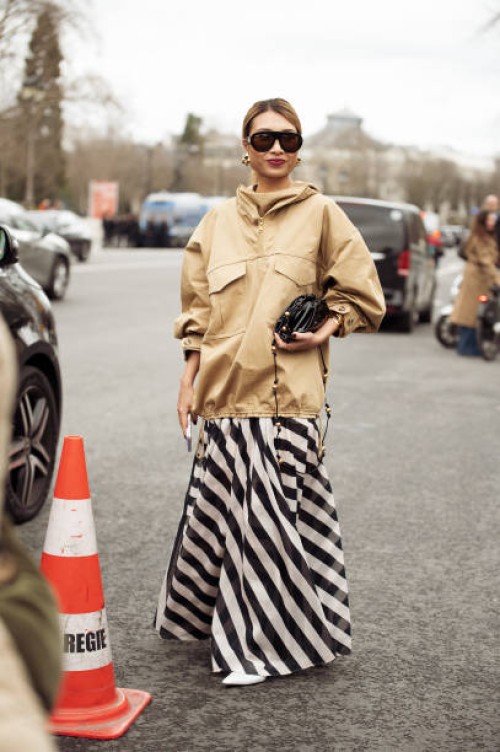 Rosie Lai wears a beige jacket, black and white striped maxi skirt, white shoes, black and gold studded bag and black sunglasses outside the...