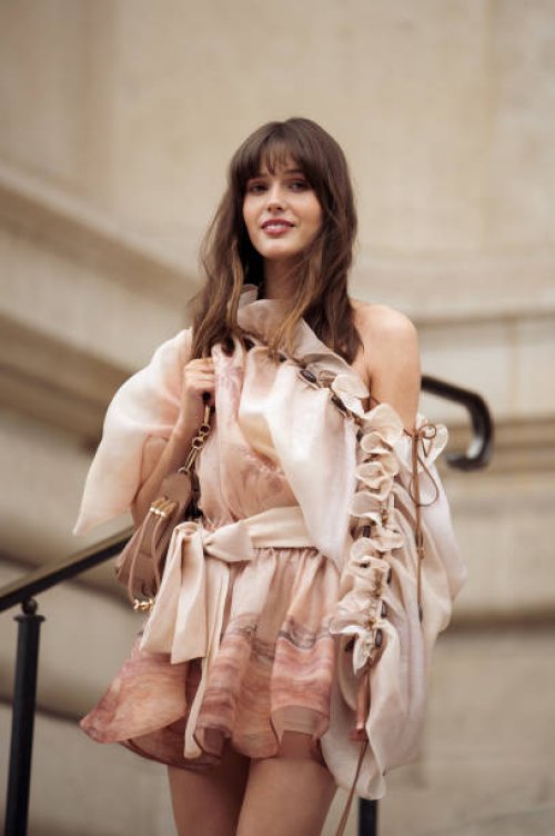 Ruby Sear wears a brown leather bag and a beige asymmetrical ruffles printed Zimmermann dress outside the Zimmermann fashion show during the...