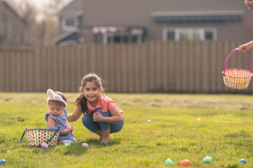 süßes kleines mädchen hilft jüngeren schwester mit ostereiersuche - garden decoration stock-fotos und bilder