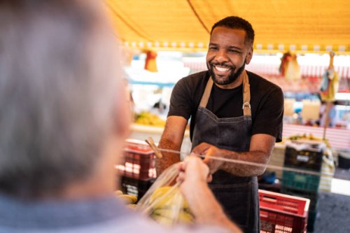 salesman helping the his customer putting the bananas in a plastic bag on a street market - food stock pictures, royalty-free photos & images