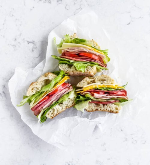 sandwiches with salami, ham, cheese, and tomatoes on parchment paper on white background - junk food stock pictures, royalty-free photos & images