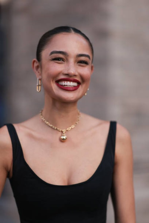 Sara Sampaio is seen wearing yellow-gold earrings a necklace from Tiffany & Co., HardWear Collection and a sleeveless, round-necked, black midi dress...
