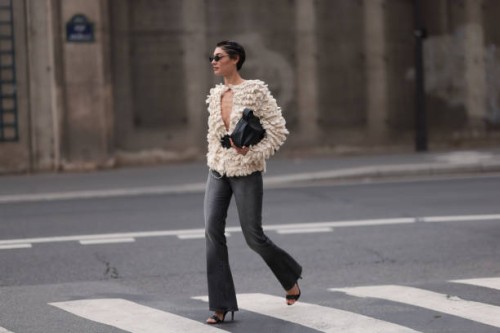 Sarah Posch is seen wearing rimless oval sunglasses with thin black metal temples and nose bridge, a beige chunky-knitted cardigan with fluffy...