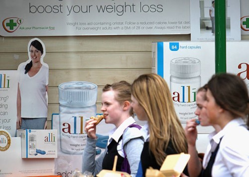 Schoolgirls eat fast food as they walk past a chemist stocking the Alli slimming pill on April 23, 2009 in Edinburgh, Scotland. The slimming pill,...