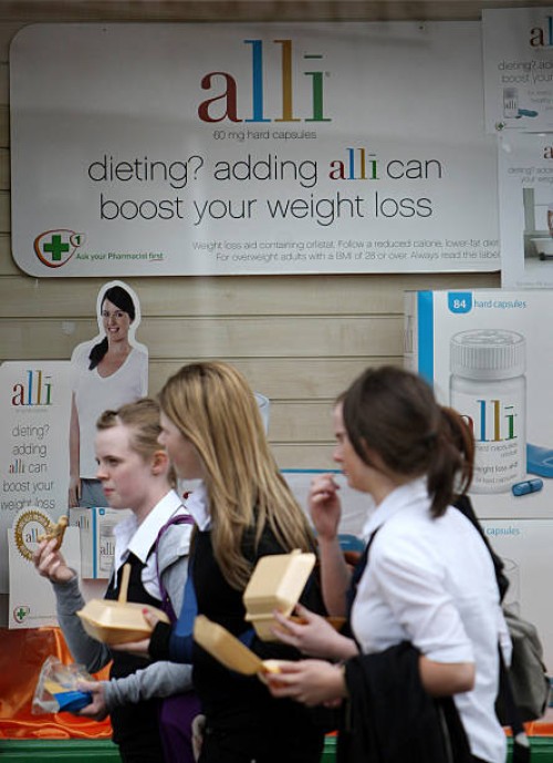 Schoolgirls eating fast food walk past a chemist stocking the Alli slimming pill on April 23, 2009 in Edinburgh, Scotland. The slimming pill, now...