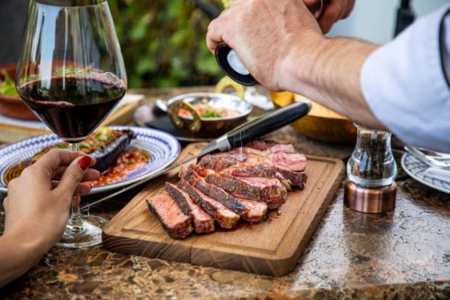 seasoning medium rare steak with salt grinder, cut on wooden board on restaurant table - food stock pictures, royalty-free photos & images