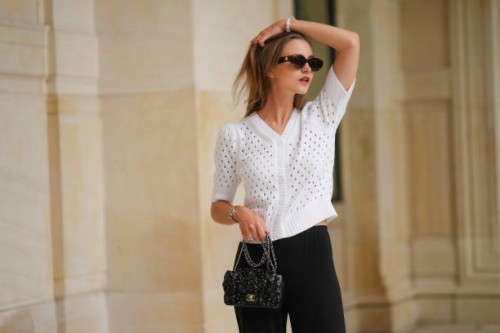 Segolene Hyppolite wears sunglasses, a white wool cardigan / top from Agnes B, a white flower shaped bracelet, a Chanel bag with floral texture /...