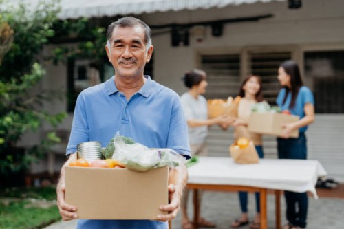 senior asian volunteer holding a box of donated groceries at food bank - food stock pictures, royalty-free photos & images