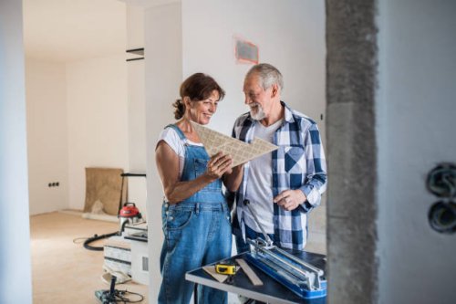senior couple laying tile floor in new home, using manual cutter. - home decoration stock pictures, royalty-free photos & images