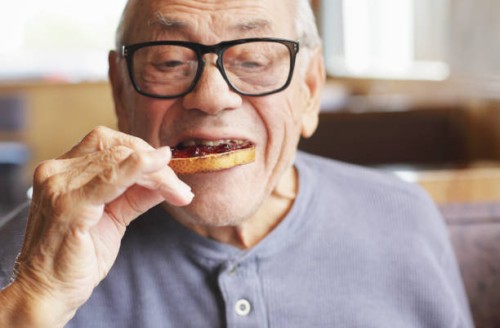 senior man eating toast and jelly jam - food stockfoto's en -beelden