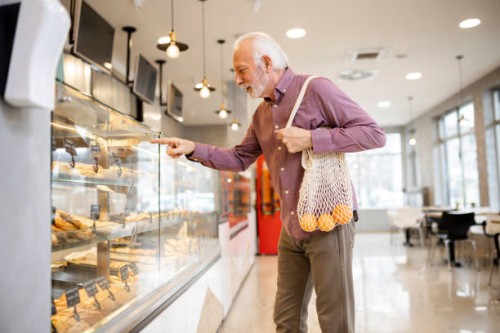 senior man looking at pastry from display cabinet of bakery - junk food stock pictures, royalty-free photos & images