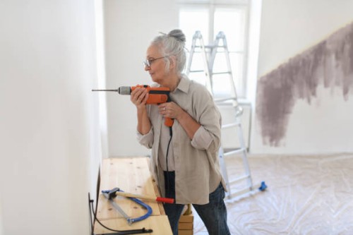 senior woman drilling into wall, preparation for hanging pictures. - home decoration stock pictures, royalty-free photos & images