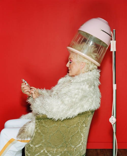senior woman sitting under hairdryer using mobile phone, side view - hairstyle stock-fotos und bilder
