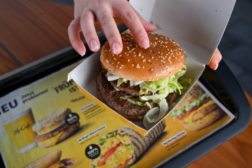 September 2024, Berlin: A woman holds a Burger M in her hands at the opening event of the McDonalds branch in Alboinstraße. The M consists of two...