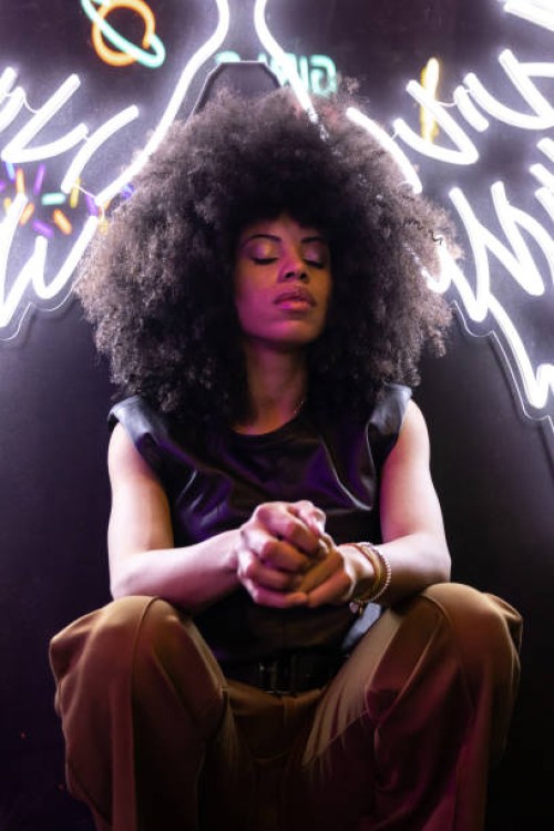 serene african american female with closed eyes sitting on hunkers under bright wings shaped illumination - fashion photos et images de collection
