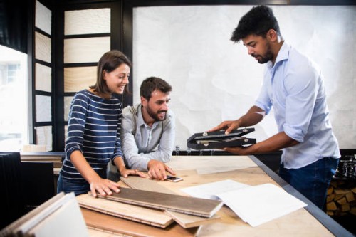 shop seller bringing a small black display case to the table with two customers. a couple of parquet sample planks, a catalog and a smart phone are on the table - home decoration stock pictures, royalty-free photos & images