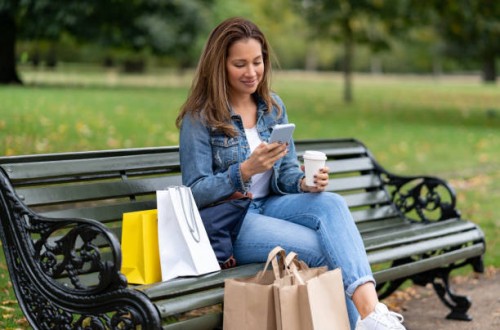 shopping woman sitting at the park drinking coffee and texting on her phone - junk food stock pictures, royalty-free photos & images