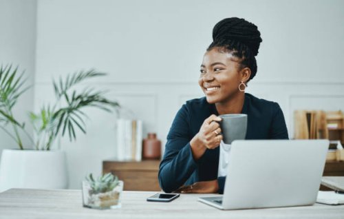 shot of a young businesswoman using a laptop and having coffee in a modern office - coffee stockfoto's en -beelden