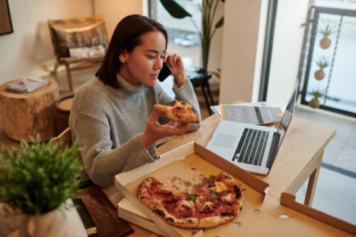 shot of a young woman enjoying some pizza while using her smartphone to make a phone call - junk food stock pictures, royalty-free photos & images