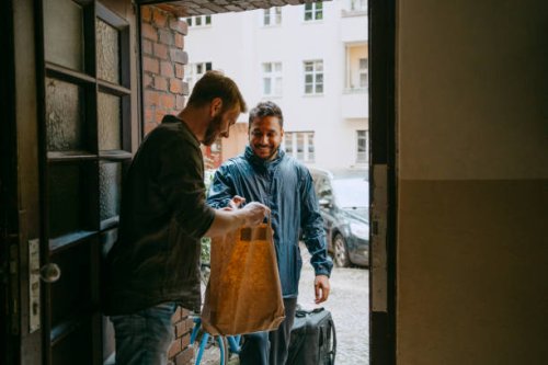 side view of man receiving parcel from delivery person while standing at doorway - food stock pictures, royalty-free photos & images
